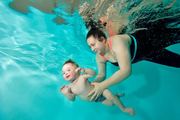 Щаслива мама і дитина з синдромом Дауна плавають разом під водою в бірюзовому басейні. Жінка підтримує дитину руками і посміхається. Портрет. Горизонтальна орієнтація . Стокове Зображення