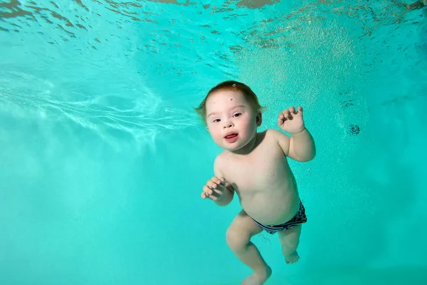 Portrait d'un enfant handicapé heureux avec le syndrome de Down qui nage et joue sous l'eau dans une piscine d'eau turquoise. Gros plan. Orientation horizontale. — Photo