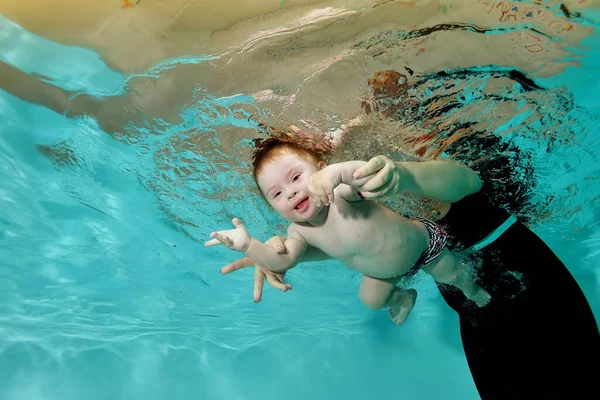 Uma criança com síndrome de Down está envolvida em esportes aquáticos e nada com sua mãe debaixo d 'água em uma piscina infantil com água azul. Deficiência infantil. Conceito. Retrato. Orientação horizontal. — Fotografia de Stock