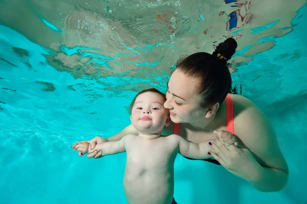 행복 한 가족: 다운 증후군 이 있는 어머니와 자녀는 청록색 물웅덩이에서 물 속에서 헤엄치는 것을 즐긴다. 그 여자는 아기를 바라보며 미소를 지으며 손을 잡고 있다. 초상화. 수평 방향. 로열티 프리 스톡 이미지