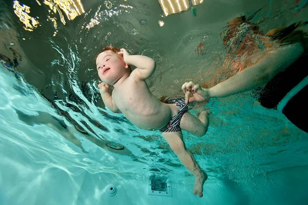 Мама вчить плавати і допомагає дитині з синдромом Дауна плавати під водою в дитячому басейні з блакитною водою. Дитяча інвалідність. Портрет. Стрілянина знизу. Горизонтальна орієнтація . Ліцензійні Стокові Фото