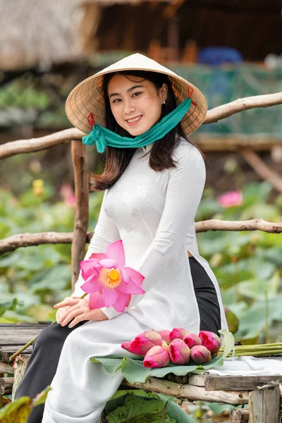 大きな蓮の湖 ベトナム アイサンや東南アジアの旅行コンセプトで木製の橋の上を歩くピンクの蓮を保持する伝統的なベトナムの帽子を持つ美しいベトナムの女性の肖像画 — ストック写真