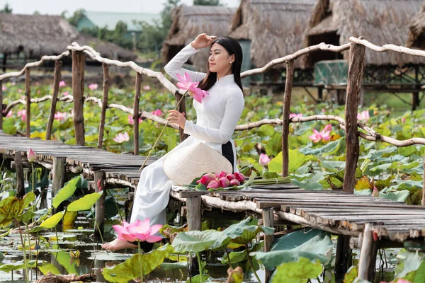 大きな蓮の湖 ベトナム アイサンや東南アジアの旅行コンセプトで木製の橋の上を歩くピンクの蓮を保持する伝統的なベトナムの帽子を持つ美しいベトナムの女性の肖像画 — ストック写真
