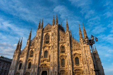 Sunset Scene of The ornate gothic facade, soaring spires and magnificent marble towers of the Duomo, Milan's monumental cathedral under big blue Lombardy skies