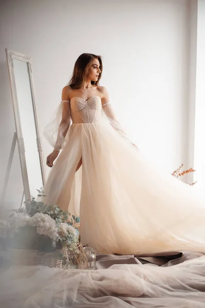 Romantic atmosphere of the bride\'s morning. Tender bride in a wedding dress colour of champagne looks out the window