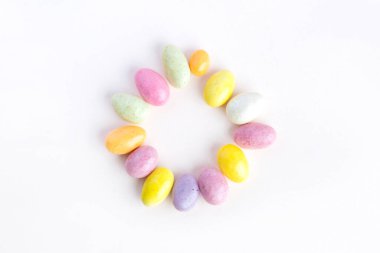 Easter circle made up of sweet colored chocolates. Delicate pastel pink background