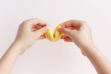 Girls hands open Fortune cookie on a pastel pink background. Chinese tradition