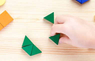 Renkli bloklarla oynayan bir çocuk, açık tahta arka planda bir model oluşturur.