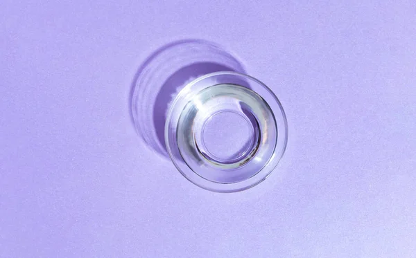 Water in a transparent cup for cats and dogs on a purple background.