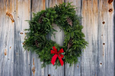 Yıpranmış ahşap arka planda kırmızı kurdeleli bir tatil çelengi..