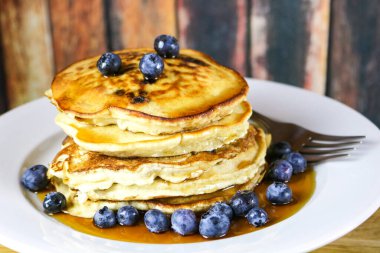 Stack of pancakes topped with fresh blueberries and maple syrup.