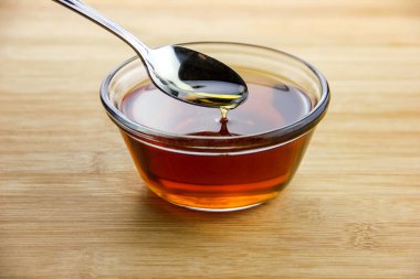 Maple syrup dripping off of a spoon into a glass bowl set on a bamboo wooden surface