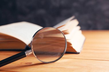 Masanın üzerinde bir kitap ve büyüteç var.