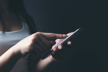 Genç bir kız elinde telefonla dikiliyor.