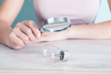 Kadın elinde büyüteçle ampule bakıyor.