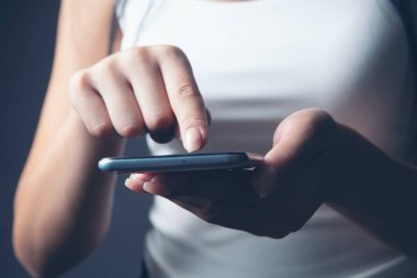 Genç bir kız elinde telefonla dikiliyor.
