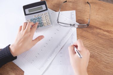 Genç bir kadın hesap makinesine güvenir ve kağıtlara not alır.