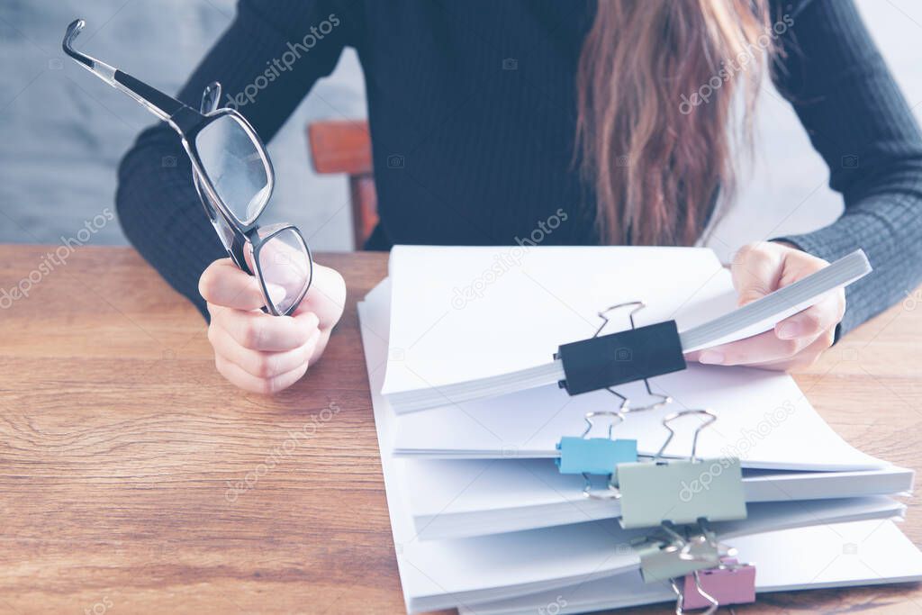 young woman in the office examines documents and holds glasses