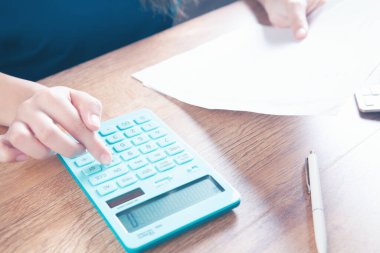 Genç bir kadın hesap makinesine güvenir ve kağıtlara not alır.