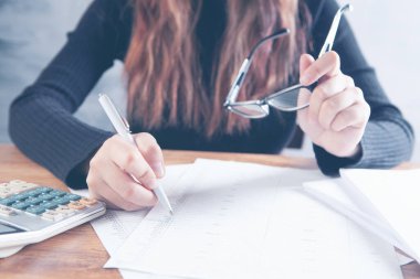 Genç bir kadın gözlük tutuyor ve kağıtlara not alıyor.