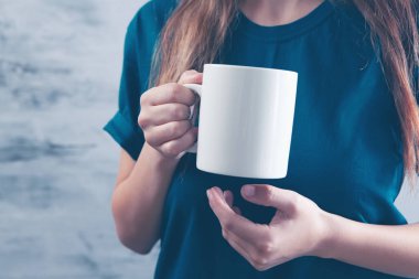 Genç bayan elinde bir fincan çayla ayakta duruyor.