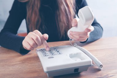 Bir kadın ev telefonundaki bir numarayı çevirir.