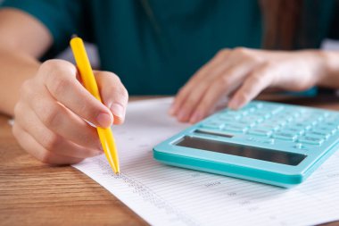 Genç bir kadın hesap makinesine güvenir ve kağıtlara not alır.