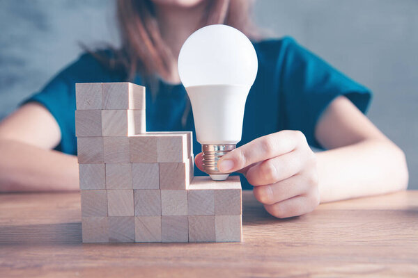 женщина держит лампочку на лестнице из деревянных кубиков