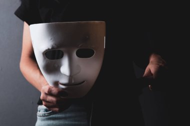 Karanlıkta elinde bıçak ve isimsiz bir maske tutan bir kadın.