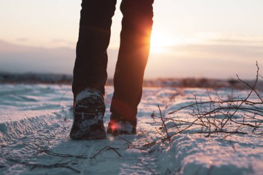 Bir adam gün batımında karda yürür..