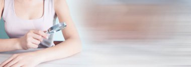 Kadın elinde büyüteçle eline bakıyor.