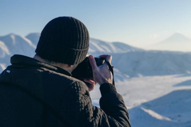 Karların altında bir dağın fotoğrafını çeken bir adam.