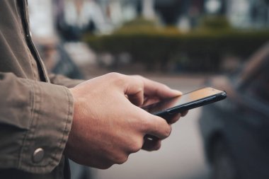 Bir adam sokakta duruyor ve telefonu kullanıyor.