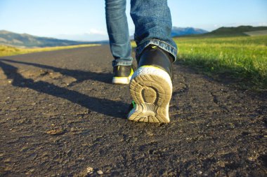 Bir adam gün batımında asfalt yolda yürür.