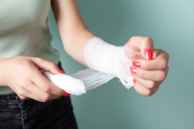 Genç esmer, yaralı koluna bandaj yapıştırıyor.