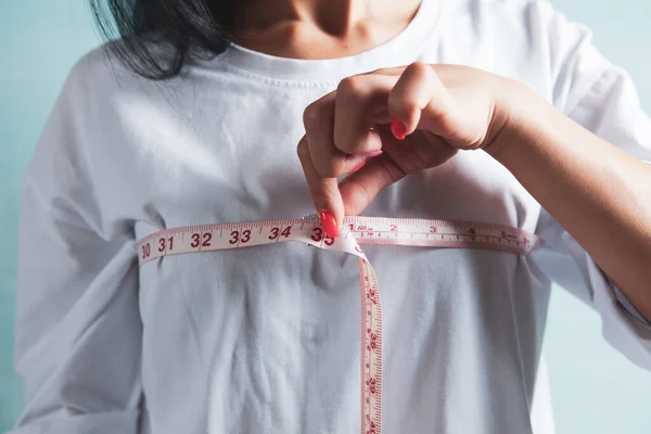 瘦小的女人用一条测量带测量她的乳房 — 图库照片