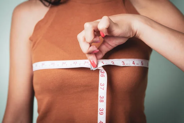 瘦小的女人用一条测量带测量她的乳房 — 图库照片