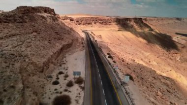 Mavi gökyüzünün çöl kumlarında asfalt yolda giden araba, beyaz bulutlar.
