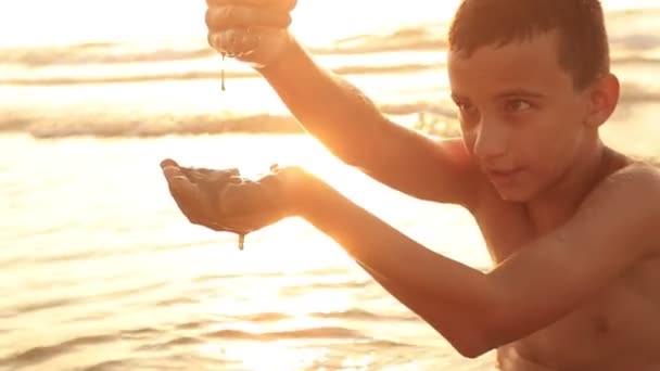 晚上，男孩在沙滩上用小鹅卵石做东西。夏天快乐的童年 — 图库视频影像