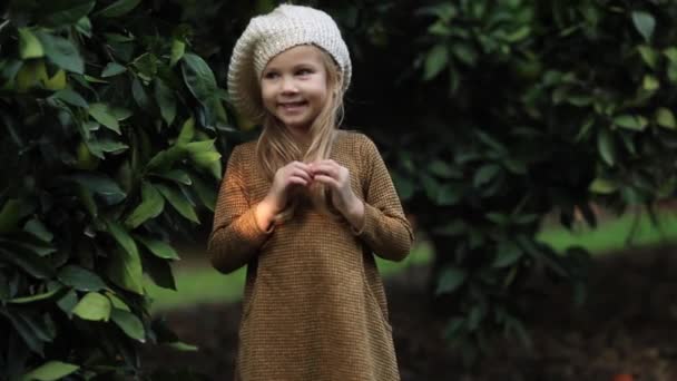 Encantadora niña con cesta de mimbre llena de naranjas de pie en el jardín verde sonriendo a la cámara — Vídeo de stock