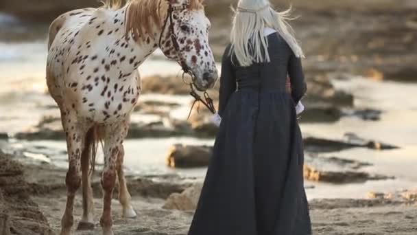 妈妈和女孩穿着雅致的衣服，骑着美丽的斑点马走在岩石海岸上。治疗 — 图库视频影像