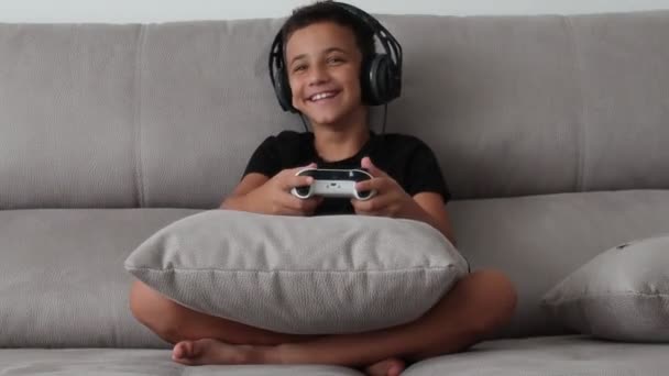Băiat zâmbind și distrându-se jucând un joc video cu controlere pe o canapea — Videoclip de stoc