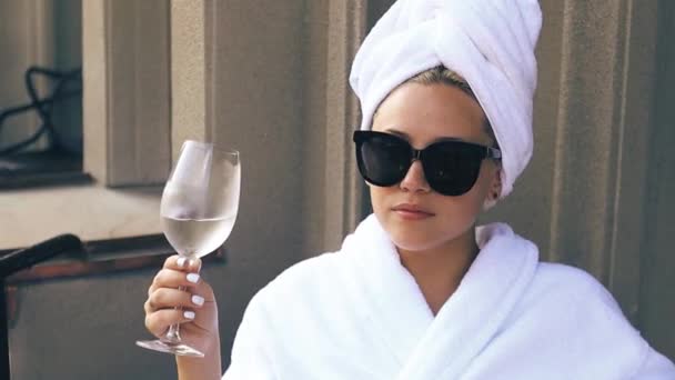 Pengantin wanita pirang cantik dengan jubah mandi putih dan kacamata hitam menikmati segelas sampanye — Stok Video
