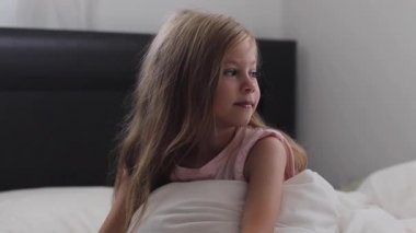 çocuk bir gülümseme ve sevinç ile uyanır. Bebeği yatakta yudumluyor. Beyaz yatakta günaydın.