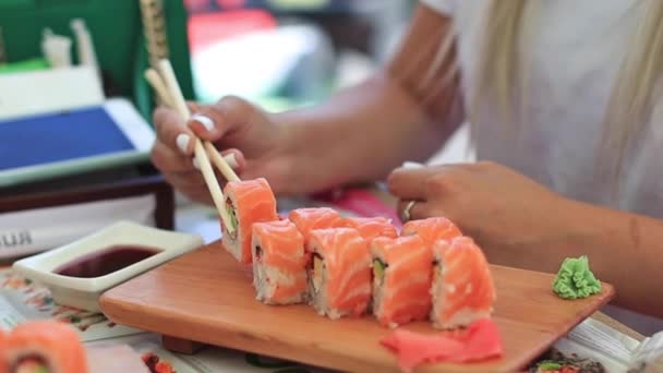箸で女性の手のクローズアップショットは、醤油にセットされたスタイリッシュに置かれた寿司をダンクダンク — ストック動画