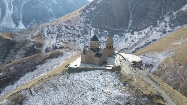 Vista aérea de la naturaleza en Georgia. Montañas del Cáucaso, Iglesia de la Trinidad de Gergeti situada en la cima de una colina, vegetación, valle, pueblo en el fondo — Vídeo de stock
