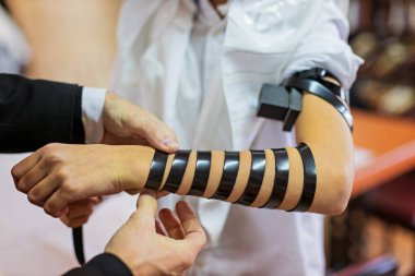 Detail of a moment when a Jewish rabbi puts tefillin on the arm of a thirteen year old boy to say a prayer before the bar mitzvah clipart