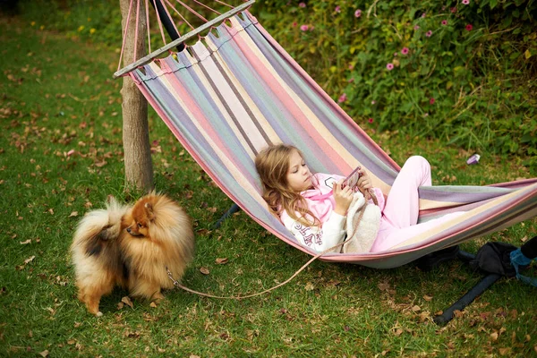 Child girl lying in a hammock and playing games on a smartphone in the summer — 스톡 사진