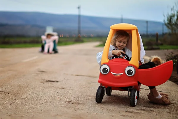 Little adorable toddler girl driving big vintage toy car and having fun with playing outdoors. Gorgeous happy healthy child enjoying warm summer day. Smiling stunning kid playing — Foto de Stock