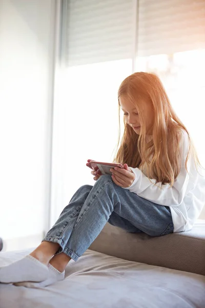 Ребенок проверяет социальные сети с помощью смартфона дома. Девочки расслабляются, играя в мобильные игры — стоковое фото